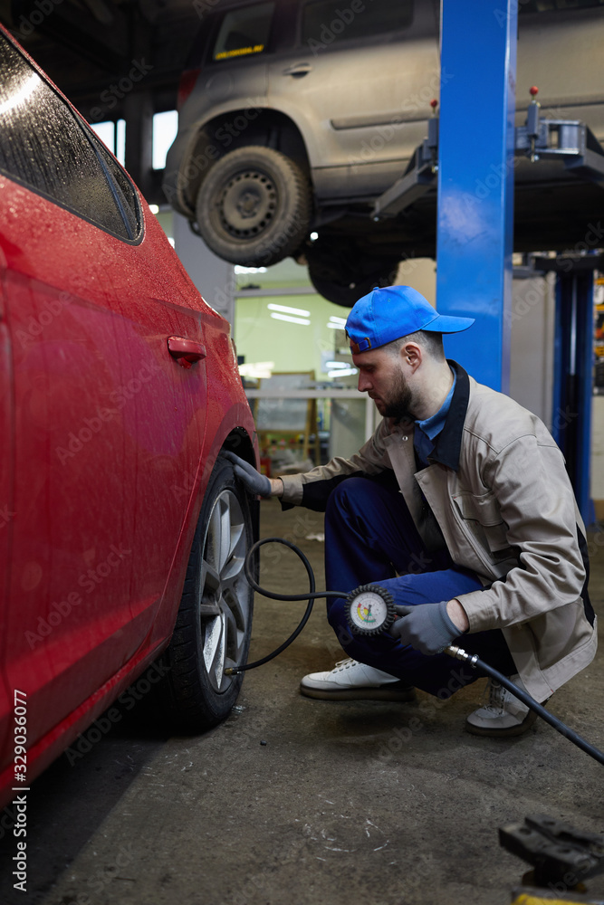 Φωτογραφία Vertical side view shot of professional repairman sitting in front of car wheel