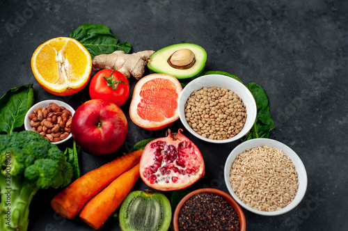 Selection of healthy food: fruits, seeds, cereals, superfoods, vegetables, leafy vegetables on a stone background. Healthy food for humans. Copy space for your text.