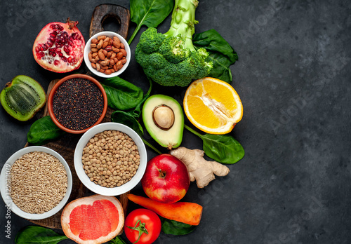 Selection of healthy food:  fruits, seeds, cereals, superfoods, vegetables, leafy vegetables on a stone background. Healthy food for humans. Copy space for your text.