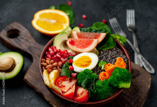 Bowl of Buddha,quinoa, orange, avocado, grapefruit, tomato, pomegranate, spinach, carrots, broccoli, egg in a bowl on a stone background, with copy space for your text