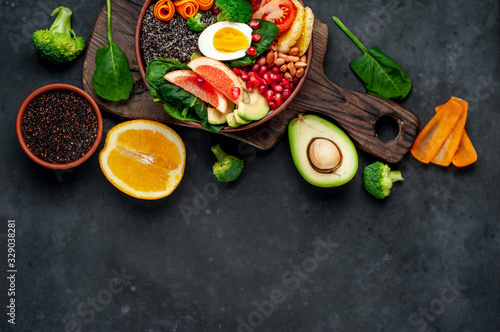 Bowl of Buddha,quinoa, orange, avocado, grapefruit, tomato, pomegranate, spinach, carrots, broccoli, egg in a bowl on a stone background, with copy space for your text