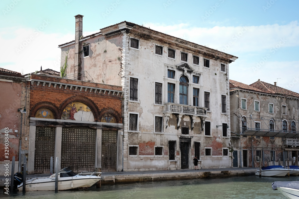 vecchio palazzo dell'isola di Murano rovinato dal tempo con cielo blu e canale della laguna Veneta