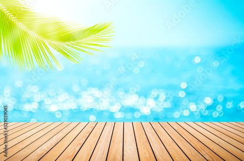 Blur tropical beach with bokeh sun light wave and palm tree on empty old wood table abstract background.