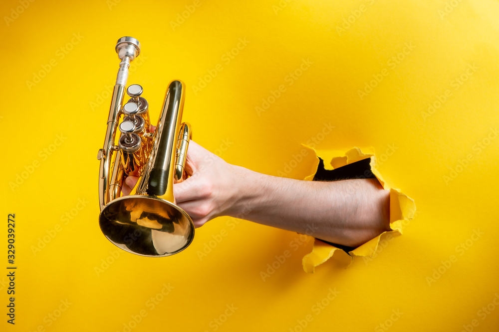 Obraz premium Hand giving a pocket trumpet through torn yellow paper background