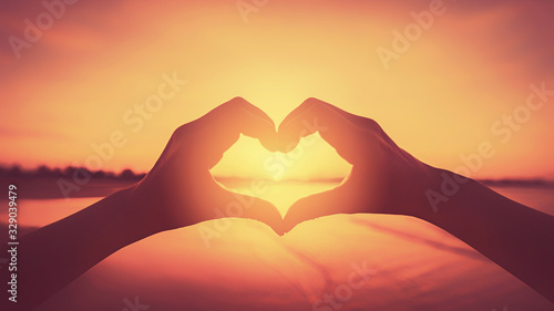 Female hands heart shape on nature bokeh sun light flare wave and blur tropical beach abstract background.