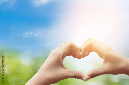 Female hands heart shape on nature green bokeh sun light flare and blur leaf abstract background.