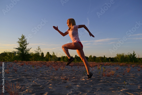 Athletic girl runs on the sand in the evening near the plants