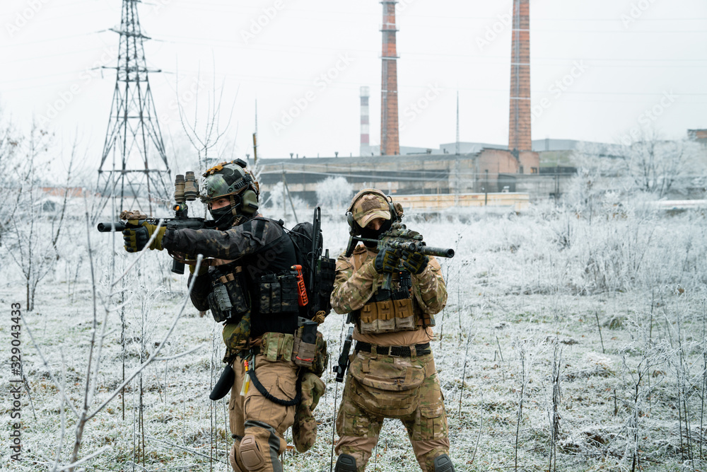 Men in camouflage cloth and black uniform with machineguns with factory on background. Soldiers with muchinegun aims aiming Men in camouflage cloth and black uniform with machineguns with factory on background. Soldiers with muchinegun aims aiming