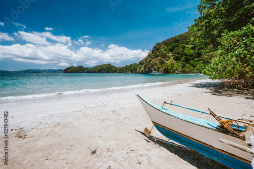 Traditional banca boat in front of remote tropical beach with exotic blue lagoon. El Nido, Philippines
