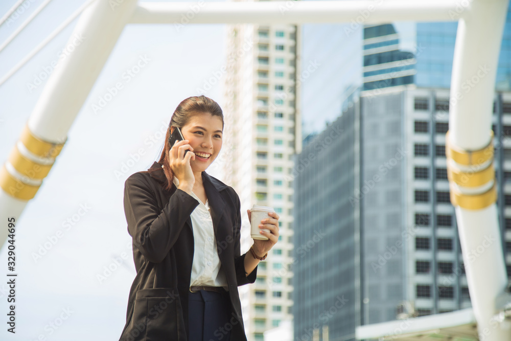 Asian woman in formal suit holding coffee cup walking outdoors talking by mobile phone. Asian woman in formal suit holding coffee cup walking outdoors talking by mobile phone.