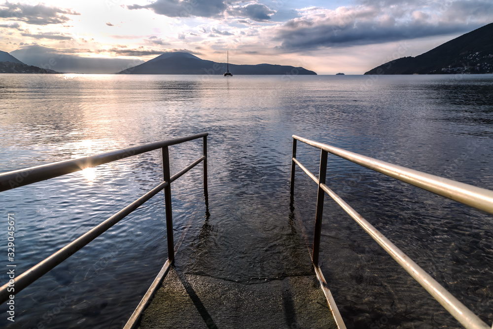 Obraz premium The pier on the sea against sunset sky and mountains in the background. Kotor Bay, Montenegro.