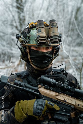 Airsoft man in black camouflage uniform with machinegun with optical sight. Soldier in the winter forest. Vertical photo.