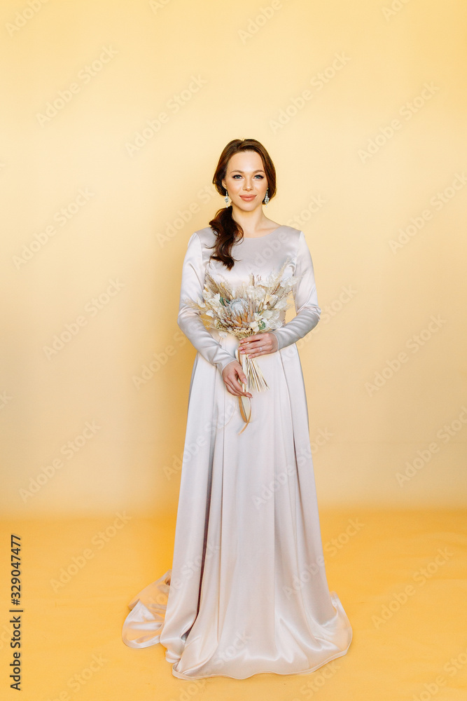 Fototapeta premium Girl in a wedding dress. Minimalism at a wedding photo shoot. Beautiful bride in the Studio on a yellow background.