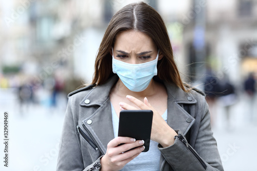 Scared girl with mask reading news on her phone on street