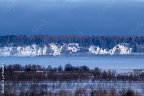 winter landscape with trees and fog over a frozen river