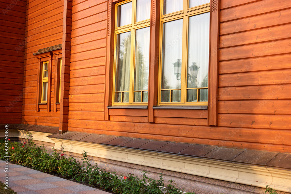 Orange wood house facade with flowers. Windows with yellow frames. Orange wood house facade with flowers. Windows with yellow frames.