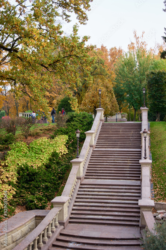 Granite stairs in autumnal park. Trees with green and yellow leaves.