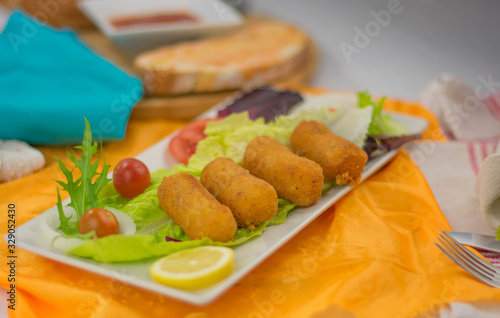 four chicken croquettes in a bowl with lettuce garnish tomatoes bread with tomato and oil