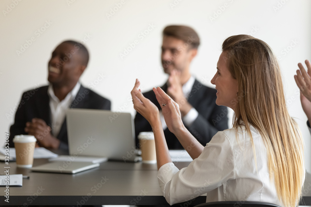 Side view head shot smiling young woman applauding to speaker, mixed race millennial colleagues team feeling joyful, celebrating great work results, company success at business meeting at office. Side view head shot smiling young woman applauding to speaker, mixed race millennial colleagues team feeling joyful, celebrating great work results, company success at business meeting at office.