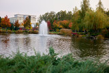 Landscape of autumn park pond and trees. Fountain in a lake.