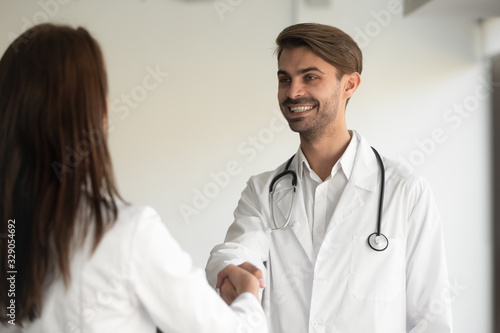 Happy young male general practitioner shaking hands with new female coworker at clinic office. Smiling doctor welcoming nurse at job. Two millennial colleagues thanking each other for cooperation.