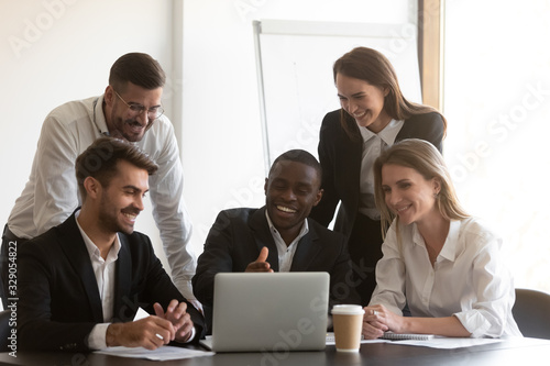 Positive african american male employee showing computer software to happy diverse coworkers at meeting. Young mixed race smiling manager explaining project results to cheerful teammates at office.