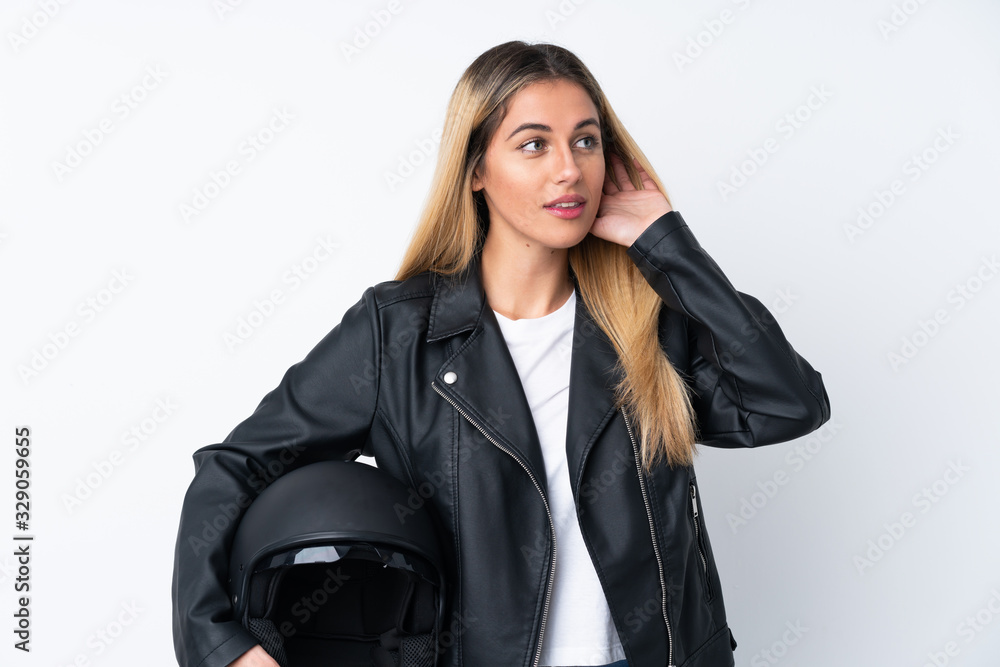 Young Uruguayan woman with a motorcycle helmet over isolated white background listening something Young Uruguayan woman with a motorcycle helmet over isolated white background listening something
