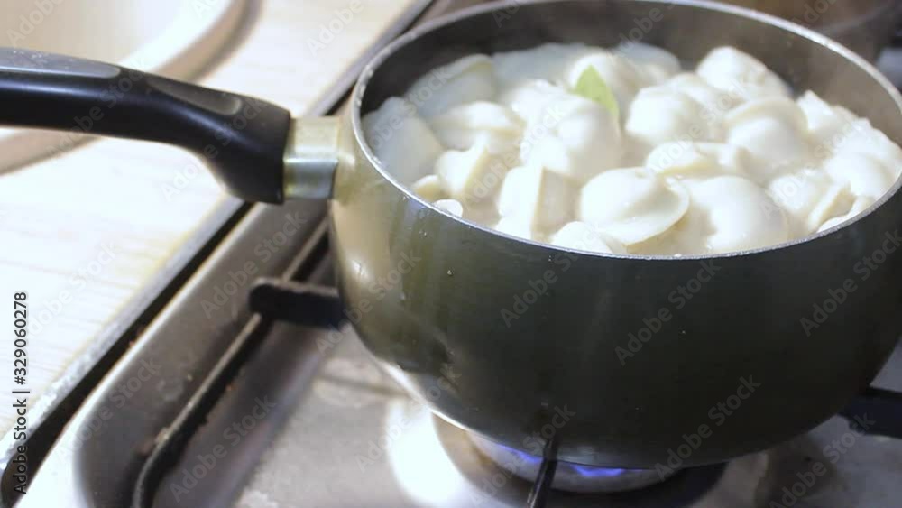 meat dumplings are cooked in boiling water in the kitchen. the chef is stirring the broth with a cooking device meat dumplings are cooked in boiling water in the kitchen. the chef is stirring the broth with a cooking device