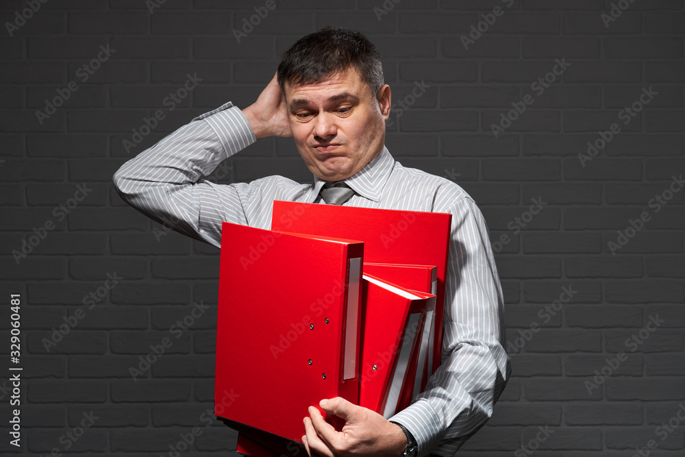 Very busy businessman closeup portrait, posing with red folders, overworking concept, dark wall background Very busy businessman closeup portrait, posing with red folders, overworking concept, dark wall background