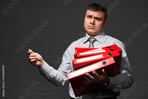 Very busy businessman closeup portrait, posing with red folders, overworking concept, dark wall background