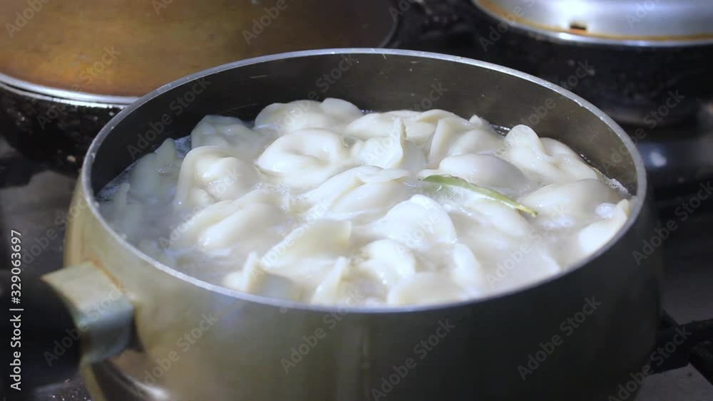meat dumplings are cooked in boiling water in the kitchen. the chef is stirring the broth with a cooking device meat dumplings are cooked in boiling water in the kitchen. the chef is stirring the broth with a cooking device