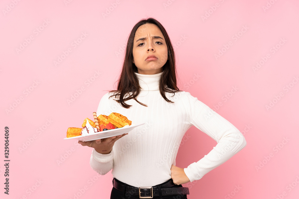 Young brunette woman holding waffles over isolated pink background angry Young brunette woman holding waffles over isolated pink background angry