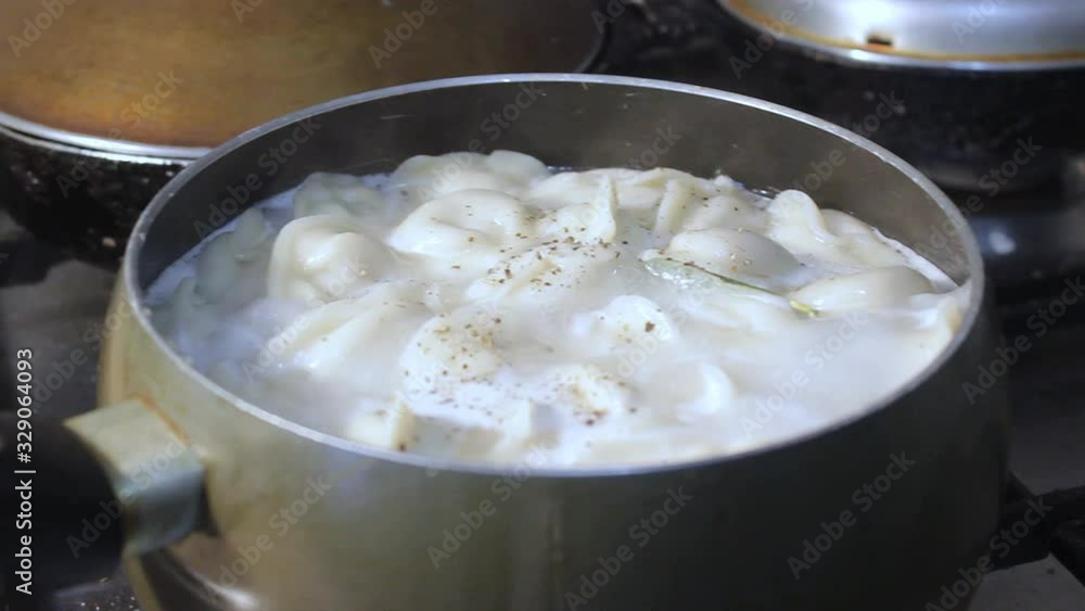 meat dumplings are cooked in boiling water in the kitchen. the chef is stirring the broth with a cooking device meat dumplings are cooked in boiling water in the kitchen. the chef is stirring the broth with a cooking device