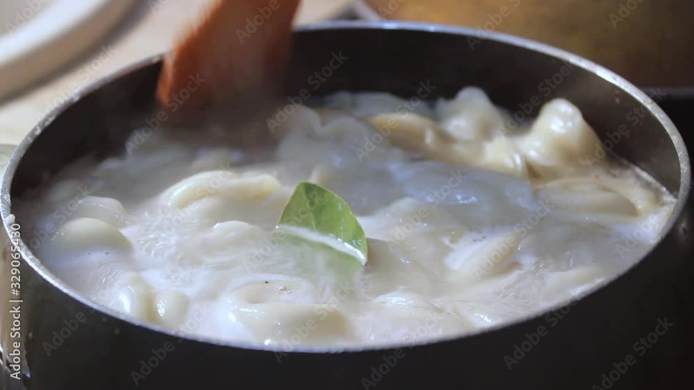 meat dumplings are cooked in boiling water in the kitchen. the chef is stirring the broth with a cooking device meat dumplings are cooked in boiling water in the kitchen. the chef is stirring the broth with a cooking device