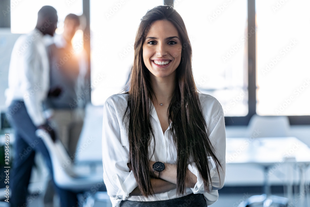 Smiling young businesswoman looking at camera while standing in the coworking space. - obrazy, fototapety, plakaty 