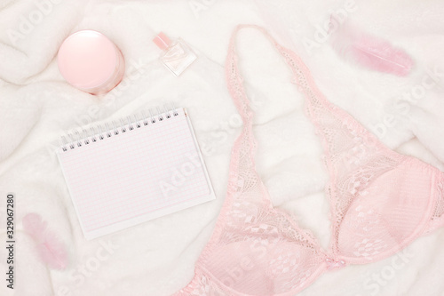 Women lifestyle concept. Lace bralette with perfume, face cream, open blank female diary on white fur, top view. Top view, flat lay
