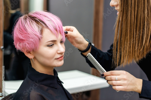 Hairdresser checking short pink hairstyle.