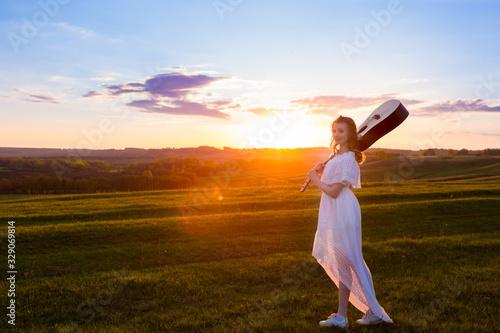 woman in dress holding the guitar on cloudy sunset sky