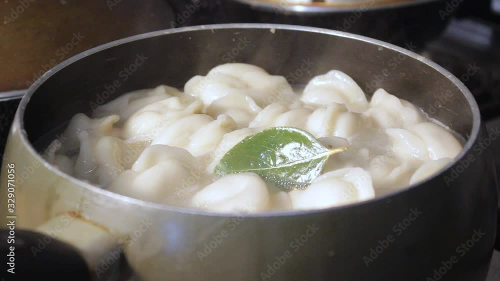meat dumplings are cooked in boiling water in the kitchen. the chef is stirring the broth with a cooking device meat dumplings are cooked in boiling water in the kitchen. the chef is stirring the broth with a cooking device