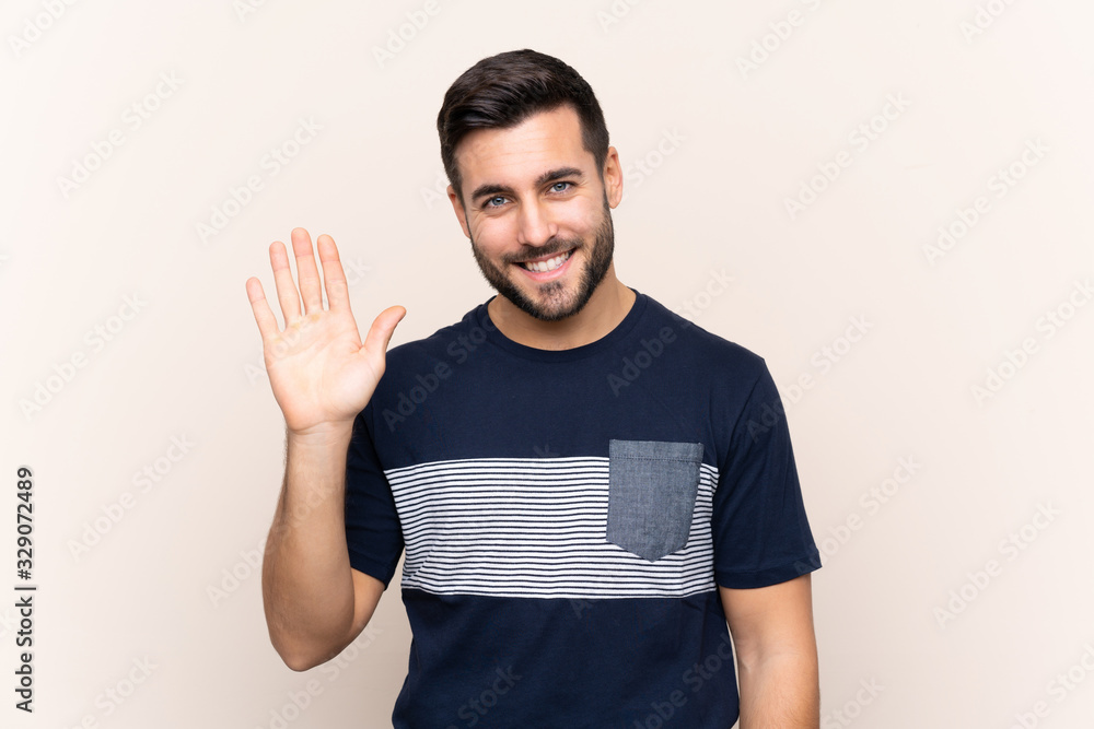 Young handsome man with beard over isolated background saluting with hand with happy expression Young handsome man with beard over isolated background saluting with hand with happy expression