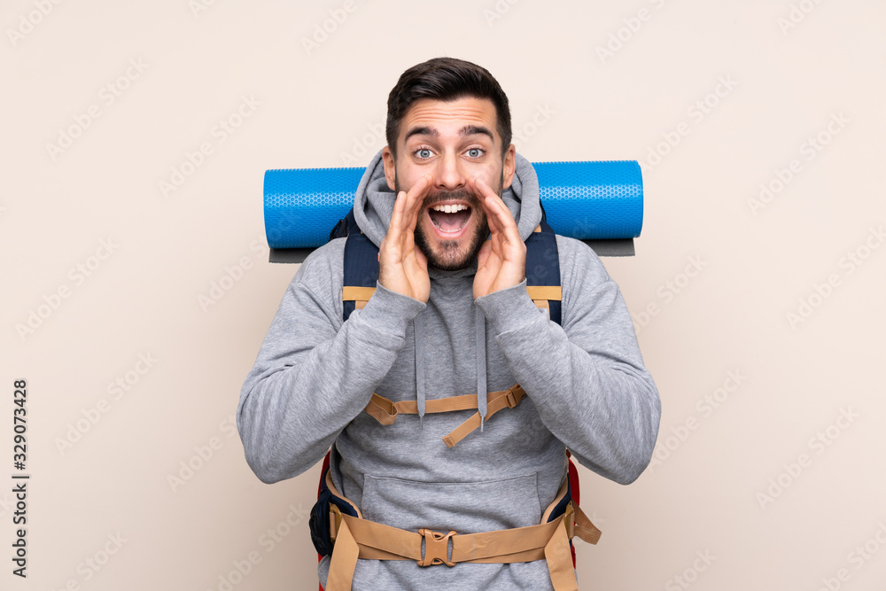 Young mountaineer man with a big backpack over isolated background shouting with mouth wide open Young mountaineer man with a big backpack over isolated background shouting with mouth wide open