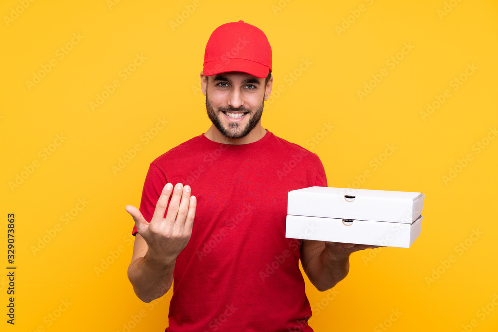 pizza delivery man with work uniform picking up pizza boxes over isolated yellow background inviting to come with hand. Happy that you came pizza delivery man with work uniform picking up pizza boxes over isolated yellow background inviting to come with hand. Happy that you came