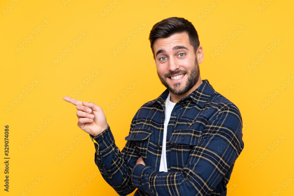 Young handsome man with beard over isolated yellow background pointing finger to the side Young handsome man with beard over isolated yellow background pointing finger to the side