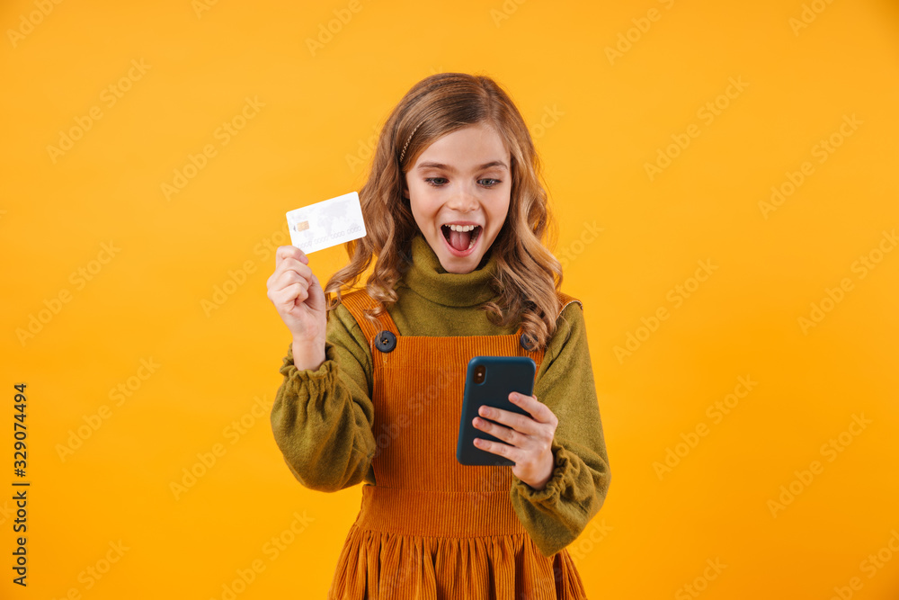 Girl child isolated over yellow wall using mobile phone