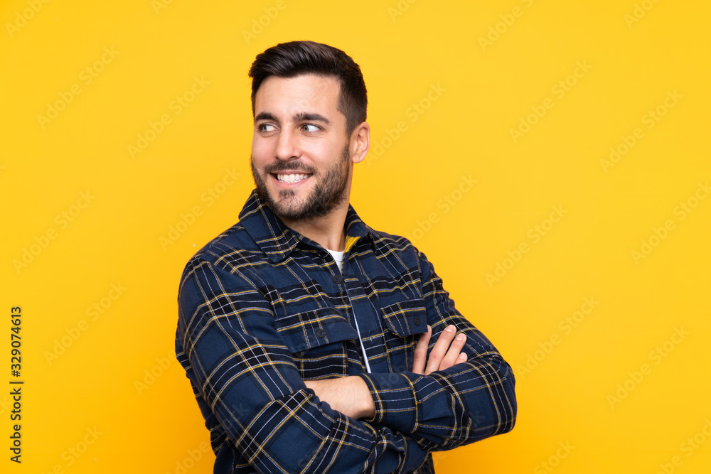 Young handsome man with beard over isolated yellow background with arms crossed and happy Young handsome man with beard over isolated yellow background with arms crossed and happy