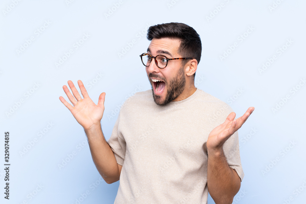 Young handsome man with beard over isolated blue background with surprise facial expression Young handsome man with beard over isolated blue background with surprise facial expression