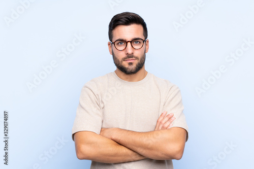 Young handsome man with beard over isolated blue background keeping arms crossed