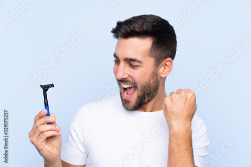 Young handsome man shaving his beard over isolated background celebrating a victory