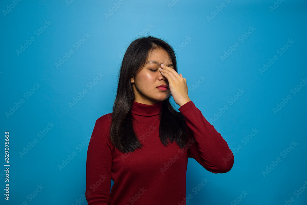 Portrait of Young beautiful asian women with blue isolated background, rubbing nose and eyes feeling fatigue and headache, stress and frustration gesture Portrait of Young beautiful asian women with blue isolated background, rubbing nose and eyes feeling fatigue and headache, stress and frustration gesture