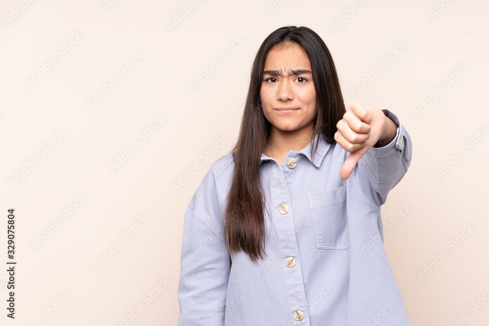 Young Indian woman isolated on beige background showing thumb down with negative expression Young Indian woman isolated on beige background showing thumb down with negative expression
